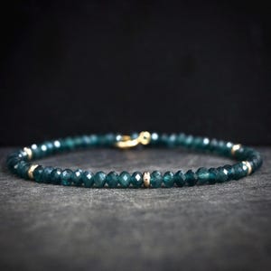 Op de afbeelding: Een delicate armband gemaakt met kleine, gefacetteerde teal blauwe edelstenen en gouden accenten.