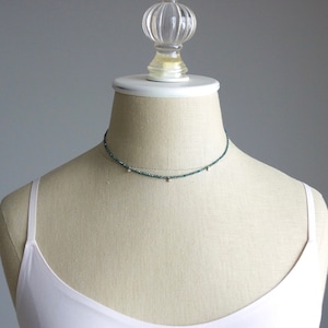 May include: A delicate choker necklace with a dark green beaded chain and small gold accents.