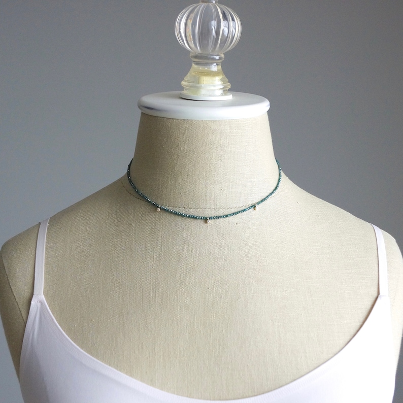 May include: A delicate choker necklace with a dark green beaded chain and small gold accents.