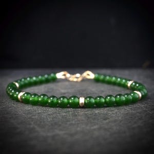 May include: A bracelet with green beads and gold-coloured details. The beads are evenly spaced, and the bracelet has a gold-coloured clasp. The jewellery item is a simple yet elegant design. The beads are a deep shade of green.