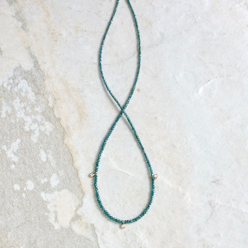May include: A delicate necklace made of blue gemstones with three small diamond accents.