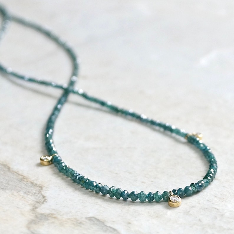 May include: A delicate necklace made of tiny blue diamonds with three larger diamonds as accents.