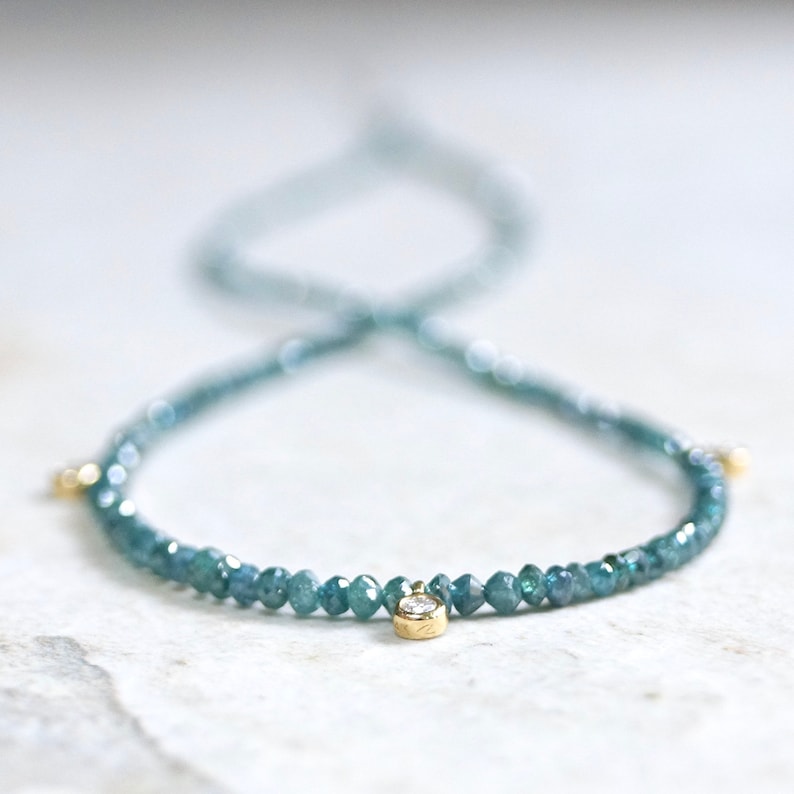 May include: A delicate necklace made of blue diamonds with a single larger diamond pendant. The necklace is made of gold and has a simple design.