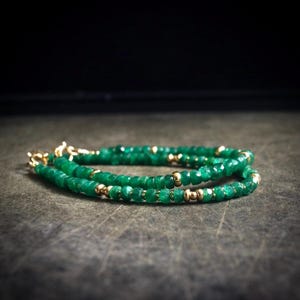May include: A beaded bracelet featuring small, faceted green gemstone beads interspersed with smooth, round gold-toned metal beads. The bracelet is arranged in a circular loop and includes a gold-toned metal lobster claw clasp at one end.