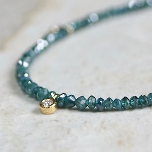 May include: A delicate bracelet made of tiny blue diamonds, with a single larger diamond charm hanging from the center. The bracelet is made of 14k gold.