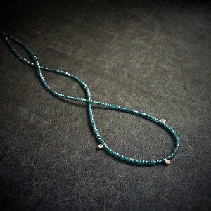 May include: A necklace made of small, dark blue beads with three small, clear stones hanging from it.