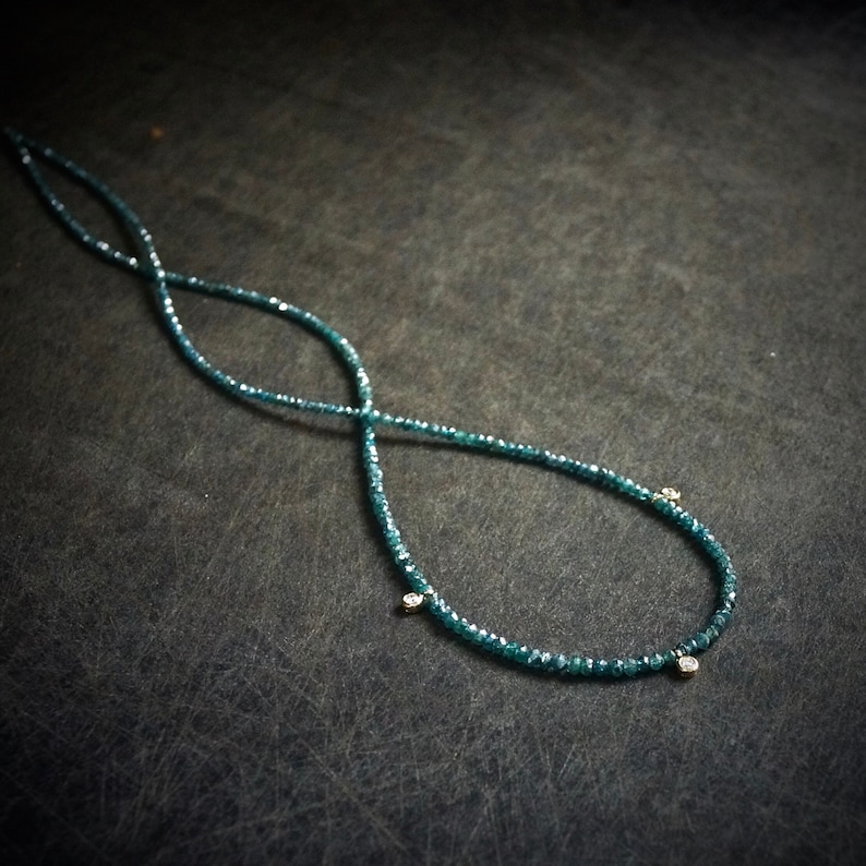 May include: A necklace made of small, dark blue beads with three small, clear stones hanging from it.