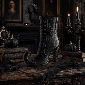 May include: A black ankle boot with a high heel and a curled toe, featuring a lace-up front and an embossed spiderweb pattern on the side and toe. The boot has a structured silhouette with decorative detailing along the top edge and heel.