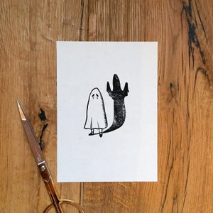 Puede incluir: Una ilustraci&oacute;n en blanco y negro de un fantasma con una cara triste y una sombra detr&aacute;s. El fantasma lleva una simple t&uacute;nica blanca y tiene brazos y piernas peque&ntilde;os.