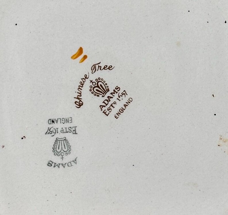Pode incluir: Close-up de uma pe&ccedil;a de cer&acirc;mica creme com as palavras "Chinese Tree" e "Adams Estd 1657 England" em escrita castanha. A pe&ccedil;a tem um emblema decorativo e &eacute; ligeiramente salpicada.