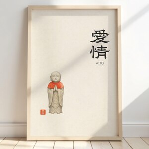 Puede incluir: Impresión enmarcada con una ilustración de un pequeño monje de piedra con un chal rojo. El fondo es crema. Hay caracteres japoneses y la palabra «AIJO» en negro. La obra de arte está enmarcada en un marco de madera clara.