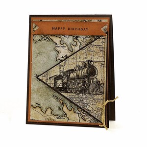 May include: A handmade birthday card with a vintage train illustration. The card features a map background and a banner that reads "HAPPY BIRTHDAY". The card is tied with twine.
