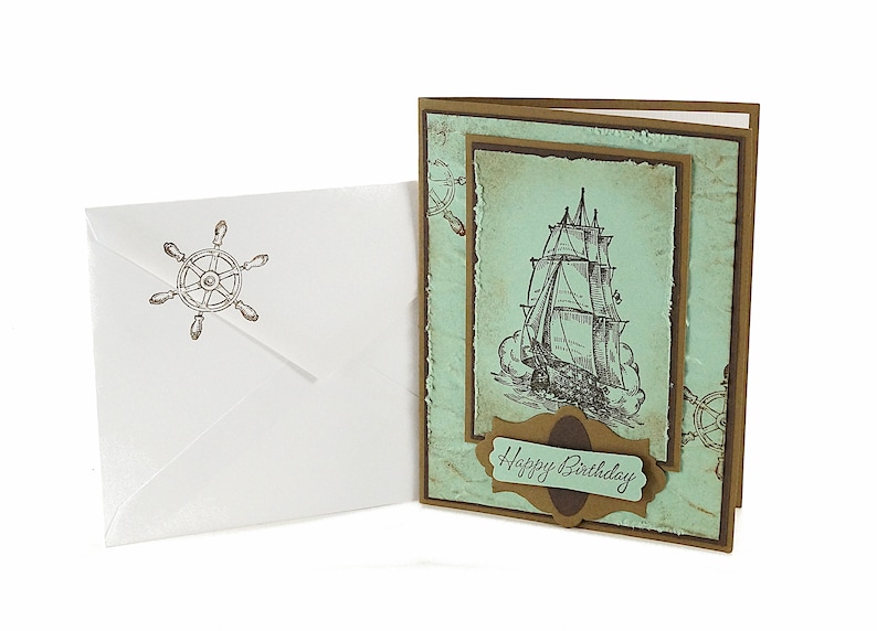 May include: A handmade birthday card with a vintage nautical theme. The card features a drawing of a ship with sails, a brown banner with the text "Happy Birthday", and a blue and green background.