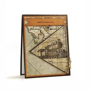 May include: A handmade Father's Day card with a vintage map and train design. The card features a brown and tan color scheme, with the words "Happy Father's Day" on a banner. A small gold twine is tied on the side.