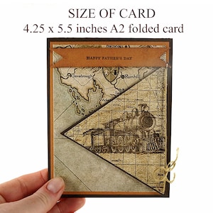 May include: A Father's Day card with a vintage map and train design. The card is 4.25 x 5.5 inches. It features a brown banner with "HAPPY FATHER'S DAY" and a sepia-toned map and train illustration. The card is held by a hand.