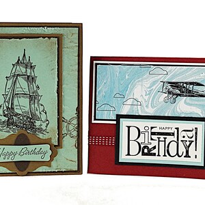 May include: Two handmade birthday cards. The first card features a vintage ship illustration with a blue and brown color scheme and the text "Happy Birthday". The second card features a vintage airplane illustration with a red, blue, and black color scheme and the text "Happy Birthday!"
