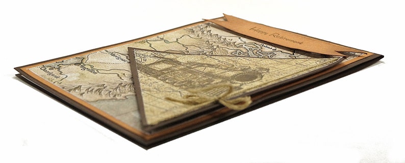 May include: A handmade retirement card with a vintage map design. The card features a layered construction with a brown and tan color scheme. A banner with "Happy Retirement" is attached. The card is tied with twine.
