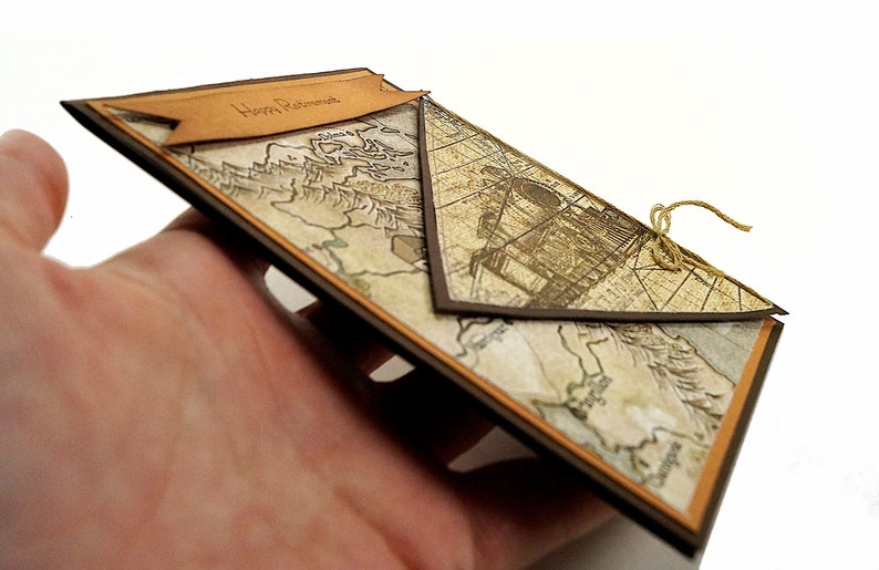 May include: A handmade retirement card with a vintage map design. The card features a brown border and a banner that reads "Happy Retirement." A twine bow secures the card's flap.