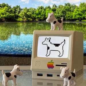 May include: A beige, retro-style computer monitor featuring a multi-colored apple logo on the front panel. The screen displays a black and white pixelated dog graphic. Three small, white dog figurines with black spots are positioned around the monitor.