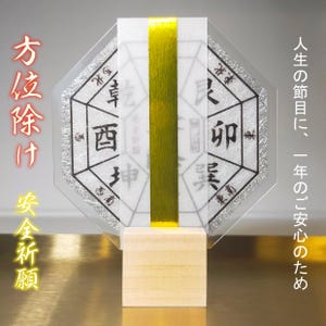 Puede incluir: Un omamori japonés, un talismán para la buena suerte, con un diseño geométrico y caracteres japoneses. El omamori se sujeta con una base de madera y una cinta dorada. El texto en el omamori dice "Oración de seguridad".