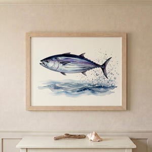 May include: Watercolor painting of a blue and purple tuna fish leaping from the ocean. The artwork is framed in a light wood frame. The fish is surrounded by water droplets, with blue waves below.
