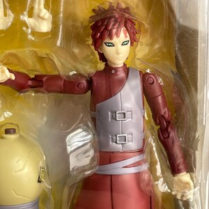 May include: A red and gray action figure of a character with spiky red hair and green eyes. The figure is in a clear plastic package, with additional interchangeable hands. The figure is wearing a red outfit with a gray vest.
