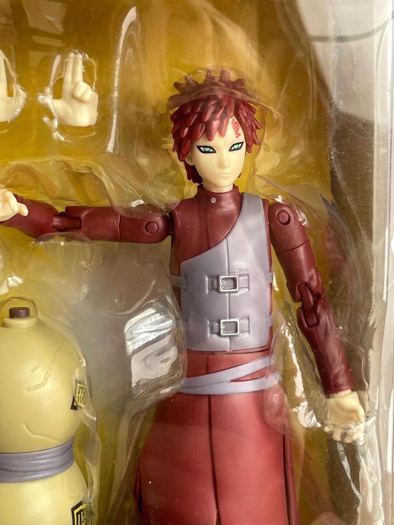 May include: A red and gray action figure of a character with spiky red hair and green eyes. The figure is in a clear plastic package, with additional interchangeable hands. The figure is wearing a red outfit with a gray vest.