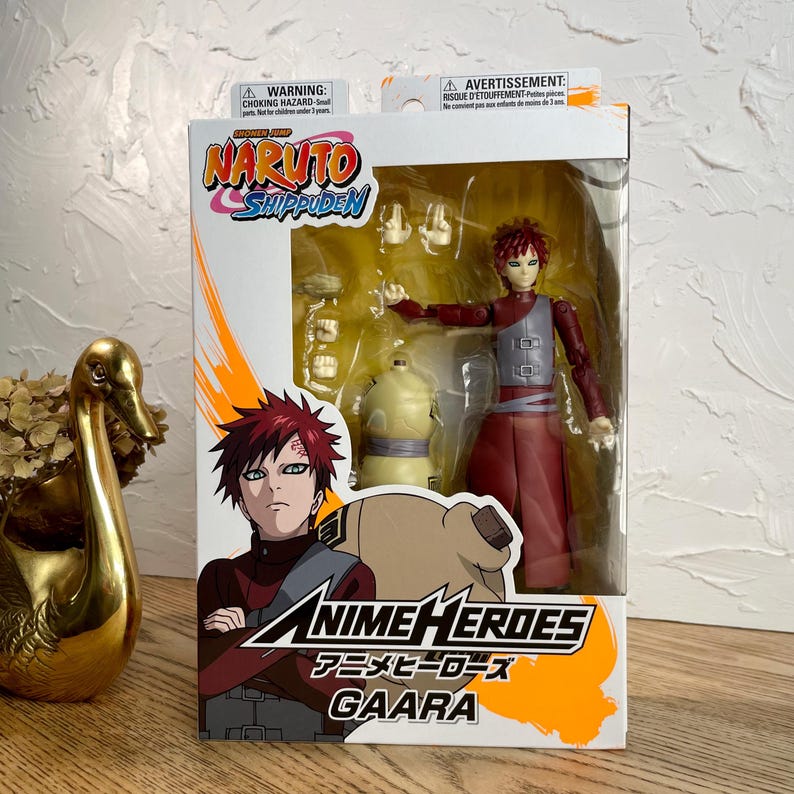 May include: A boxed Anime Heroes Gaara action figure from Naruto Shippuden. The figure is in a dynamic pose, wearing a red and gray outfit. The box features character art and the Anime Heroes logo, with warnings in English and French.