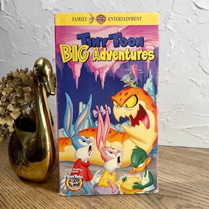 May include: A white ceramic mug with a black handle and the text "But First, Coffee" in a bold, black font. The mug is set against a blurred background, suggesting a cozy setting. The mug appears to be approximately 4 inches tall.