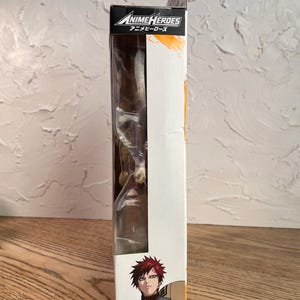 May include: A boxed Anime Heroes action figure featuring Gaara. The packaging is white with orange accents and the Anime Heroes logo. The figure is visible through a clear plastic window. The character Gaara is depicted on the box.