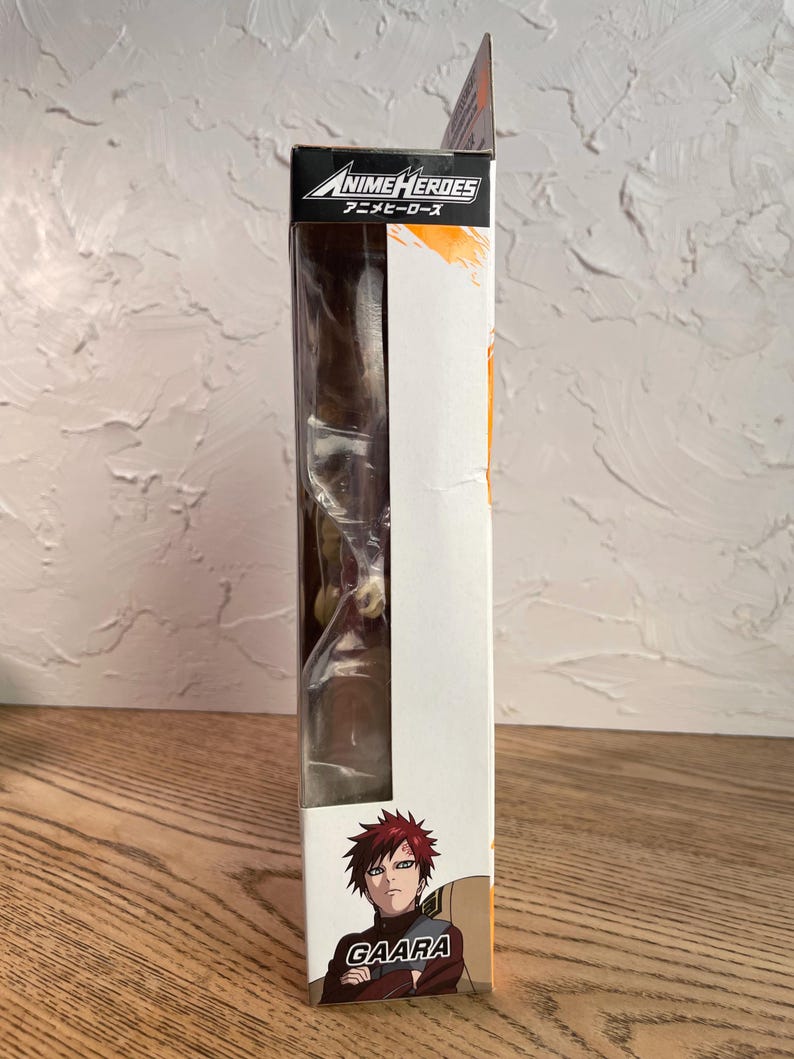 May include: A boxed Anime Heroes action figure featuring Gaara. The packaging is white with orange accents and the Anime Heroes logo. The figure is visible through a clear plastic window. The character Gaara is depicted on the box.