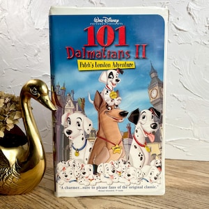 May include: A VHS tape of Disney's "101 Dalmatians II: Patch's London Adventure." The cover features a blue background with illustrations of Dalmatian dogs and London landmarks. The text on the tape reads "101 Dalmatians II" and "Patch's London Adventure."