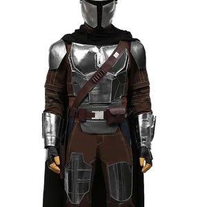 Op de afbeelding: Een full-body shot van een Mandalorian kostuum. Het kostuum heeft een zilveren helm, borstplaat en armbeschermers. Het pak heeft bruine en zwarte accenten, een zwarte cape en een gereedschapsriem. De laarzen zijn zwart.