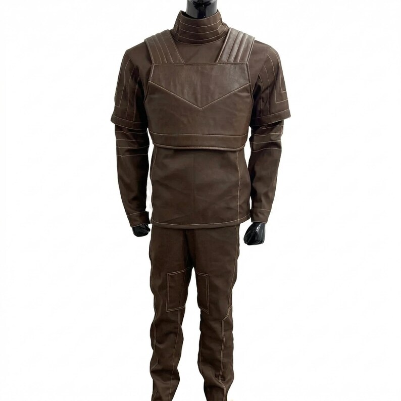May include: A brown costume comprising a high-collared top with long sleeves and trousers. The top features a layered design with a chest plate and shoulder detailing. The trousers have visible stitching and pockets. The outfit is displayed on a mannequin.