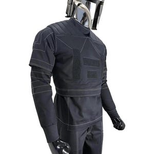 May include: A black costume with white stitching, featuring a silver helmet. The outfit includes a long-sleeved top, pants, and gloves. The top has multiple rectangular patches and a high collar. The helmet is reflective.