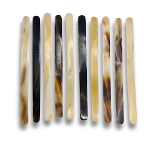 Può includere: Una collezione di dieci bastoncini lunghi, sottili e piatti disposti verticalmente in fila. Ogni bastoncino presenta una superficie liscia e lucida con vari motivi naturali in tonalità crema, beige, marrone chiaro, marrone scuro e nero.