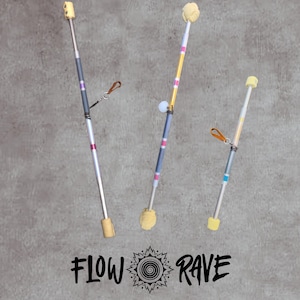 May include: Three flow wands of varying lengths featuring metallic shafts with coloured bands, cream-coloured textured ends, and attached leather loops. The text FLOW RAVE with a central spiral graphic is positioned below the wands.