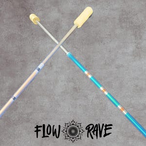 May include: Two fire flow wands crossed in an X shape, featuring metallic shafts with blue and silver sections, topped with cream-coloured wicks. The text FLOW RAVE with a central spiral sunburst icon is positioned below the wands on the surface.