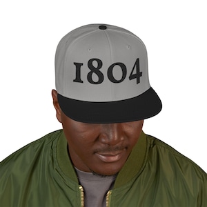 May include: A gray and black baseball cap with the number "1804" printed in large, black letters. The cap has a flat brim and a button on top. The person in the image is wearing a green jacket.