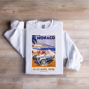 Może przedstawiać: Biała bluza z nadrukiem vintage'owego plakatu przedstawiającego samochód wyścigowy na torze w Monako. Plakat zawiera napis "Monaco" i "11 et 13 AVRIL 1936".