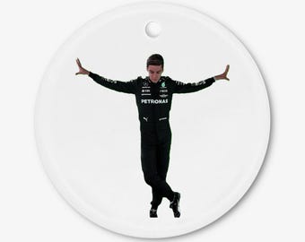 May include: White ceramic ornament featuring a person in a black racing suit with the Petronas logo, arms outstretched. The ornament has a hole at the top for hanging. The person is in a dynamic pose, suggesting movement.