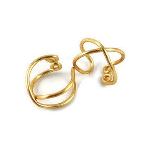 May include: Two gold ear cuffs, one with a simple double-loop design and the other with a more intricate, twisted design.