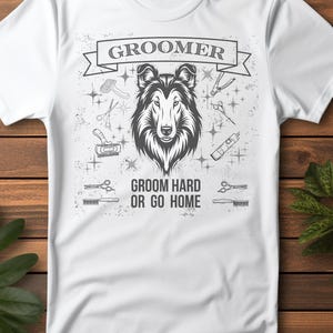 Puede incluir: Camiseta blanca con un diseño para peluqueros caninos. El diseño presenta una ilustración detallada de la cara de un perro, la palabra "GROOMER" en una pancarta y la frase "GROOM HARD OR GO HOME".
