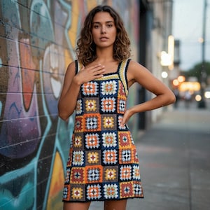 May include: A sleeveless, knee-length crochet dress with a patchwork design. The dress is made up of square motifs in various colours, including orange, blue, yellow, and brown, with black trim. It has a square neckline and thick straps.