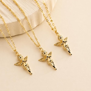 May include: Three gold-colored angel pendant necklaces. Each necklace features a delicate chain and a detailed cherub pendant with wings. The pendants are in a shiny gold finish, and the chains have a textured design.