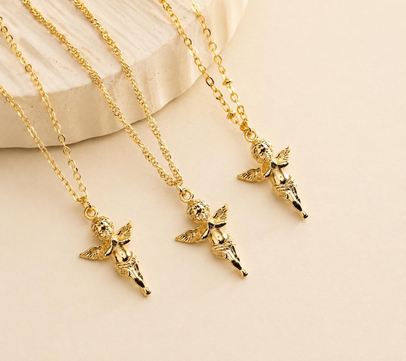 May include: Three gold-colored angel pendant necklaces. Each necklace features a delicate chain and a detailed cherub pendant with wings. The pendants are in a shiny gold finish, and the chains have a textured design.