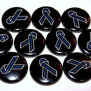 May include: A collection of ten circular pin-back buttons, each featuring a black background with a centered awareness ribbon graphic. The ribbon is black with a thin, vertical blue stripe running through the middle, outlined in white.