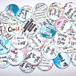 May include: A collection of colorful round buttons with inspirational quotes and floral designs. The buttons feature phrases like "Believe in Yourself", "Don't Quit", "Today is the Day", and "Walk Unafraid".