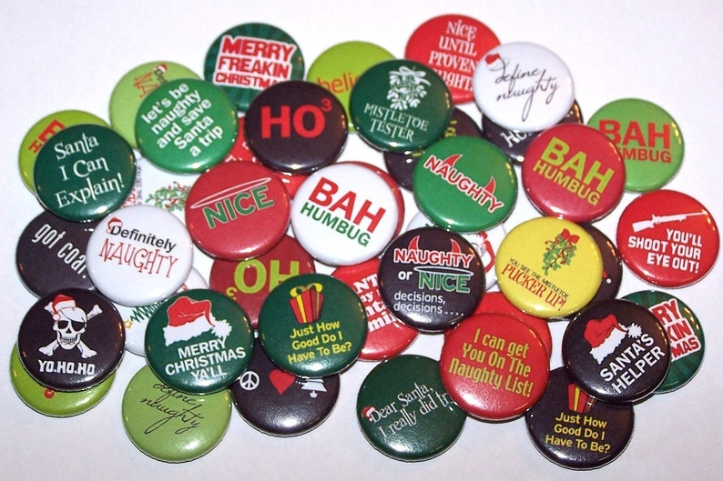 May include: A collection of 25 round Christmas themed buttons with various sayings, including "Naughty or Nice", "Bah Humbug", "You'll Shoot Your Eye Out!" and "Santa's Helper".