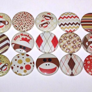 May include: A set of 15 round buttons featuring various designs with monkeys, stripes, and geometric patterns. The buttons are mostly beige and brown with red accents.